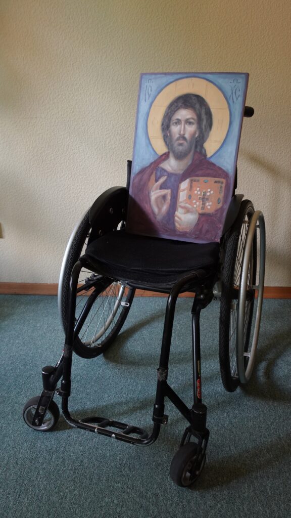 zdjęcie: wózek inwalidzki na którym znajduje się ikona Jezusa Pantokratora.